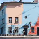 Mehrere Handwerker streichen die Fassade eines Altbaus in verschiedenen Pastellfarben mit Fassadenanstrich Premium, wobei die präzise Arbeit und die lebendigen Farbtöne die Qualität des Fassadenanstrich Premium hervorheben.