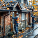Mehrere Handwerker führen an einem herbstlichen Tag Renovierungsarbeiten an den Fassaden und Dächern alter Wohnhäuser durch, umgeben von herabgefallenen bunten Blättern und nassen Gehwegen Herbstliche Renovierungsarbeiten.