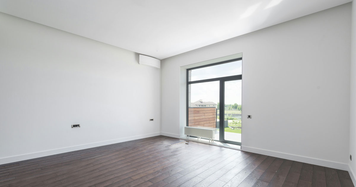Ein leerer Raum mit weißen Wänden und dunklem Holzboden als Ausgangspunkt für eine Renovierung.