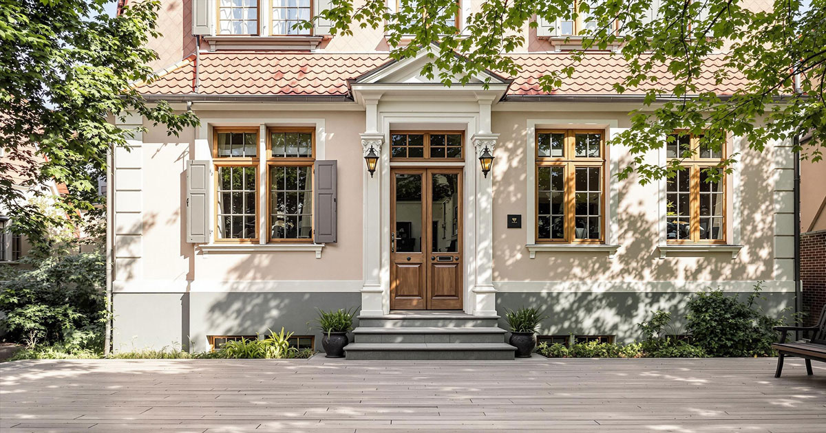Projekt 376 zeigt ein stilvolles Wohnhaus mit klassischer Fassade und Holzeingangstür umgeben von Bäumen.