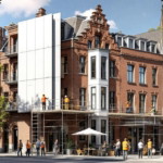 Mehrstöckiges Altbaugebäude aus rotem Backstein mit Gerüst und mehreren Handwerkern bei der Fassadensanierung im sonnigen Stadtbild, Beispiel für Serielle Wohnungssanierung Altbau.