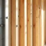 Nahaufnahme einer Ständerwand Montage aus Holzrahmen, die in einem hellen Innenraum errichtet wird, mit schraubenbefestigten Holzlatten vor einem unscharfen Wohnzimmerhintergrund.